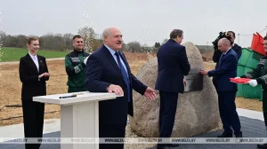 Дэпутат Алена Бераснева гатовая сустрэцца з жыхарамі Ажэшкі каб абмеркаваць будаўніцтва кафэ ў іх двары Лукашэнка на будпляцоўцы ў полі на Янкі Купалы расказвае пра заробкі ўрачоў. Справа - камень, куды заклалі "капсулу часу" з пасланнем
