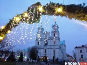 Расіян у Гродне на навагоднія святы будзе больш?  Попыт на туры ў Беларусь расце Фарный костел Гродно на Новый год в сумерках, украшенный подвесными гирляндами и зеленью.