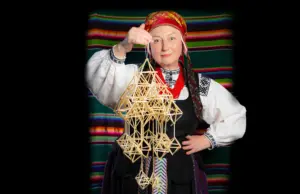 Ірына Новік з саламяным павуком-абарэгам на фоне традыцыйнай посцілкі
